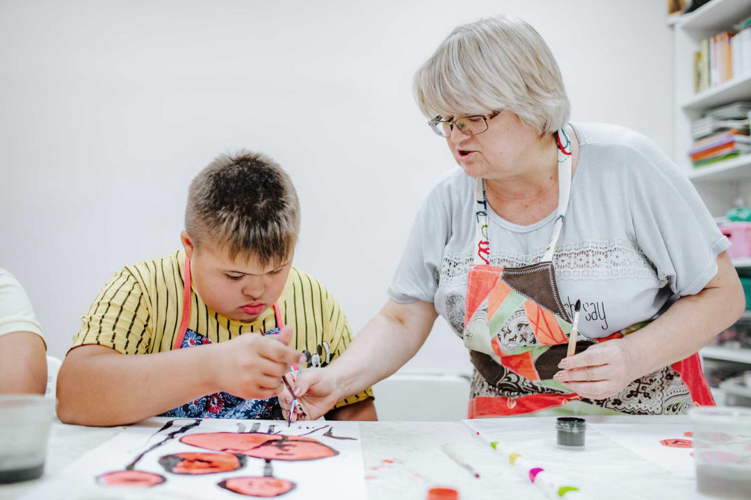 junge-mit-downsyndrom-malt-unter-anleitung